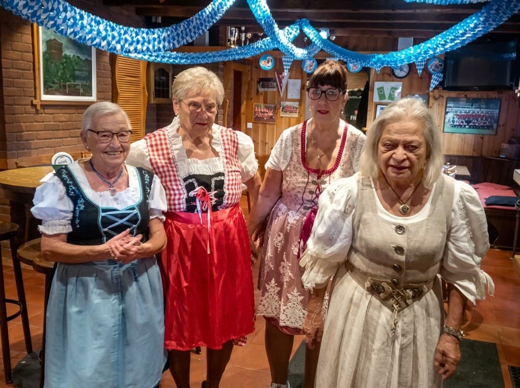 Vier Frauen in Dirndln posieren im Vereinsheim unter blau-weißen Girlanden