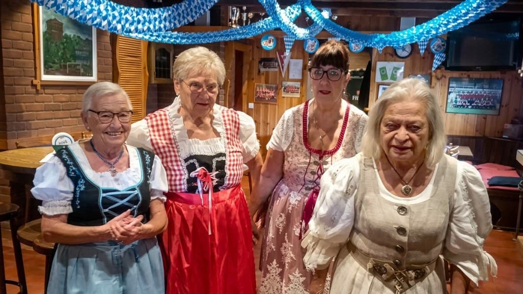 Vier Frauen in Dirndln im bayerisch geschmückten Vereinsheim mit blau-weißen Girlanden