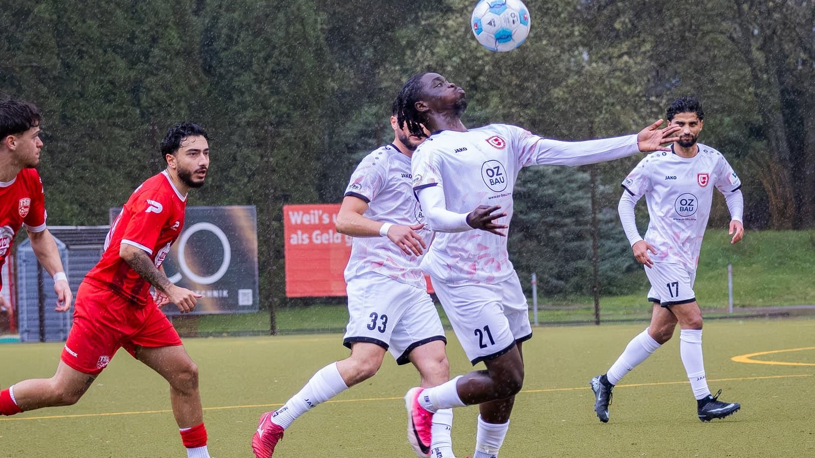 Caleb Godswill Danso nimmt im Regen den Ball mit der Brust an, dahinter Alessandro Marino und Deniz Duran sowie zwei Spieler von Türkspor Dortmund