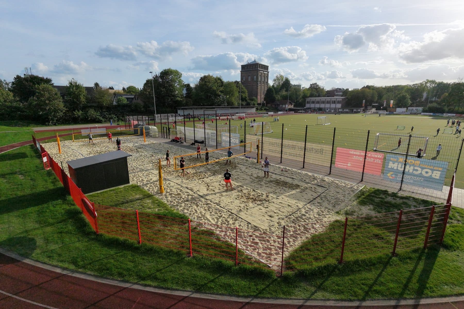 Drohnenaufnahme der beiden Beachvolleyballfelder zwischen Bäumen und Kunstrasenplatz